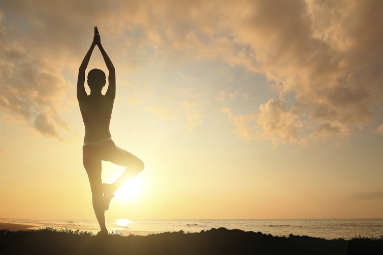 Silhueta de uma mulher jovem praticando ioga na praia com pôr do sol no horizonte