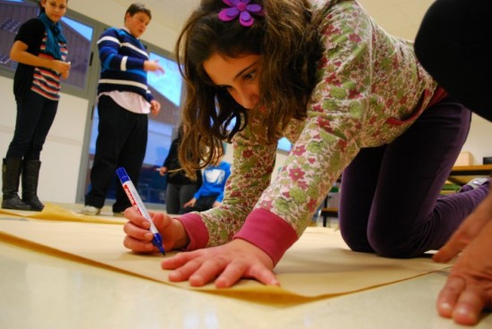 Menina autista está no chão, com uma caneta e uma cartolina, pronta para desenhar ou escrever.
