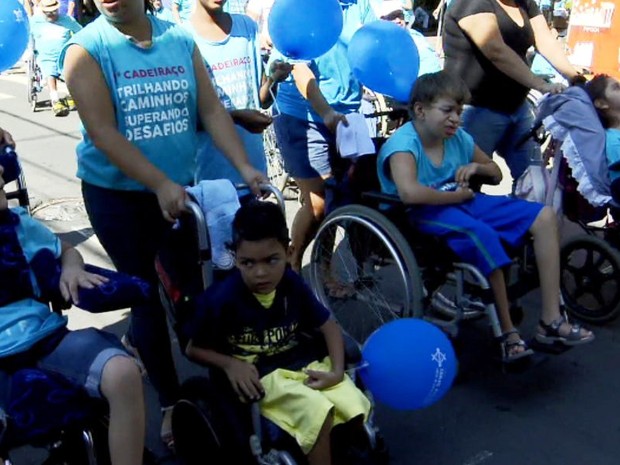 Pessoas protestam em suas cadeiras de rodas, vestindo azul e com balões de aniversário também azuis.