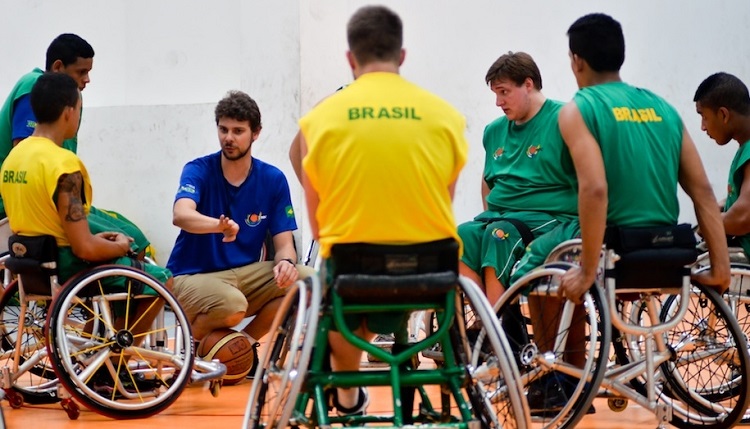 Em círculo, o técnico Tiago Frank em ginásio orienta os atletas de basquete em cadeira de rodas durante treino
