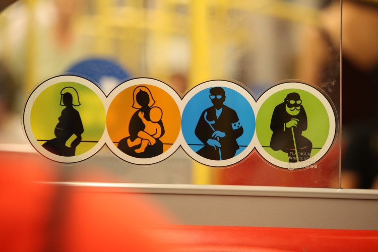 Adesivo de sinalização de assento preferencial; quatro imagens coloridas, com silhuetas dos usuários com preferência; em amarelo, uma gestante; em laranja, uma mulher com criança de colo; em azul, homem com óculos escuros e bengala, que indica deficiência visual; em verde, idoso com bengala