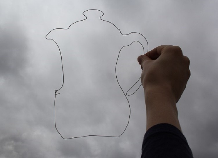 Uma mão tateia o contorno em arame no formato de um bule