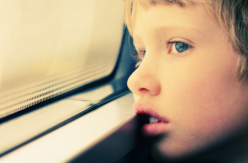 Close no rosto de uma criança, que olha distraidamente por uma janela.