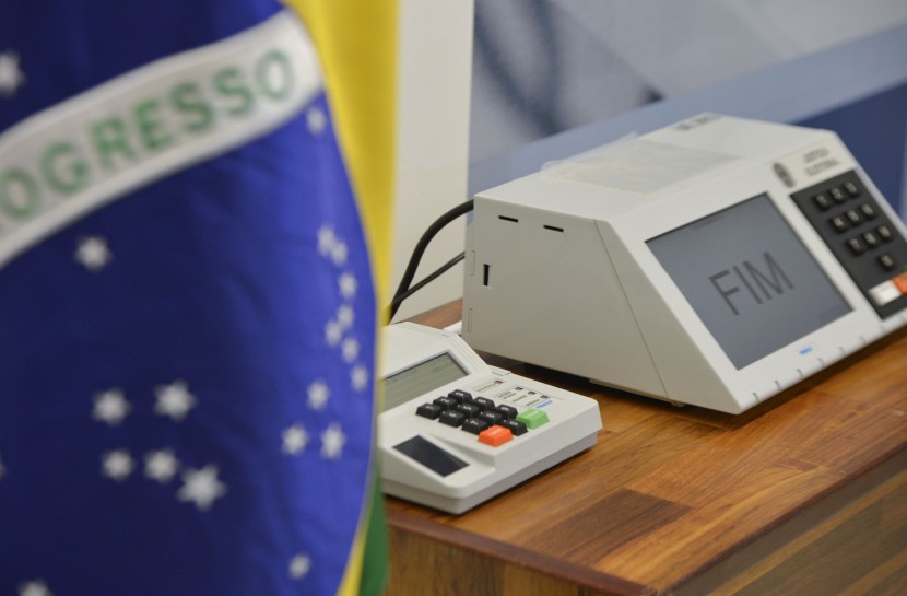 Urna eletrônica mostra, na tela, a palavra FIM, indicando o fim da votação. Ao lado esquerdo, em primeiro plano e desfocada, está a bandeira do Brasil.