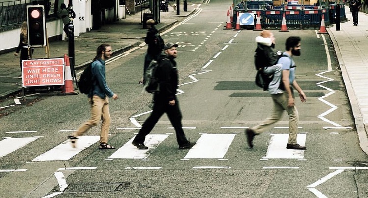Foto de três jovens atravessando a rua Abbey Road, com um rapaz menor carregado nas costas de um deles