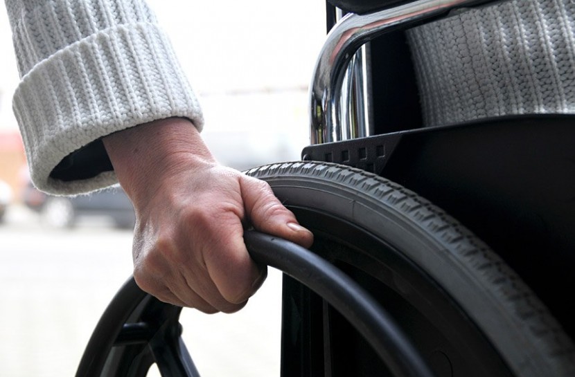 Uma mão masculina segura as rodas de uma cadeira de rodas
