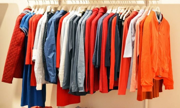 Uma arara de roupas com várias peças como camisas e jaquetas, em tonalidades de vermelho e laranja