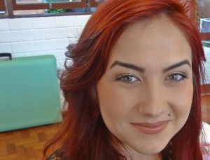 Foto de uma jovem branca com longos cabelos avermelhados e olhos claros; ela olha na direção da câmera e sorri