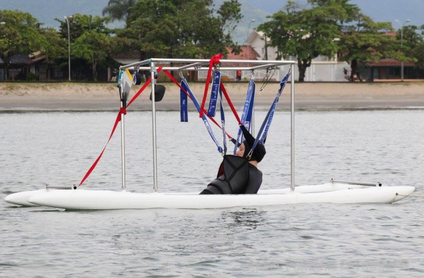 No mar, Mara Gabrilli navega em embarcação adaptada à prática esportiva. Seu corpo está suspenso com auxílio de tiras de segurança atreladas à embarcação.