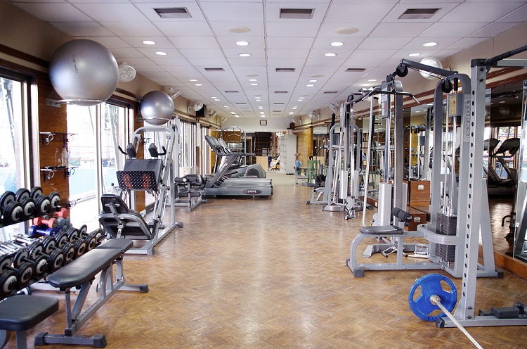 Foto de uma academia de ginástica vazia. Há vários aparelhos de musculação, com halteres e pesos de diferentes formatos e tamanhos.