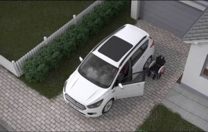 Imagem aérea de um veiculo branco estacionado, com as portas e o porta-malas abertos. Há uma cadeira de rodas próxima ao veículo