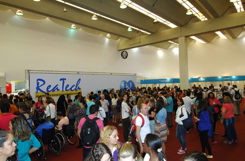 Multidão na frente da área de entrada da Reatech. No canto esquerdo da imagem, grande banner com o nome do evento Reatech.