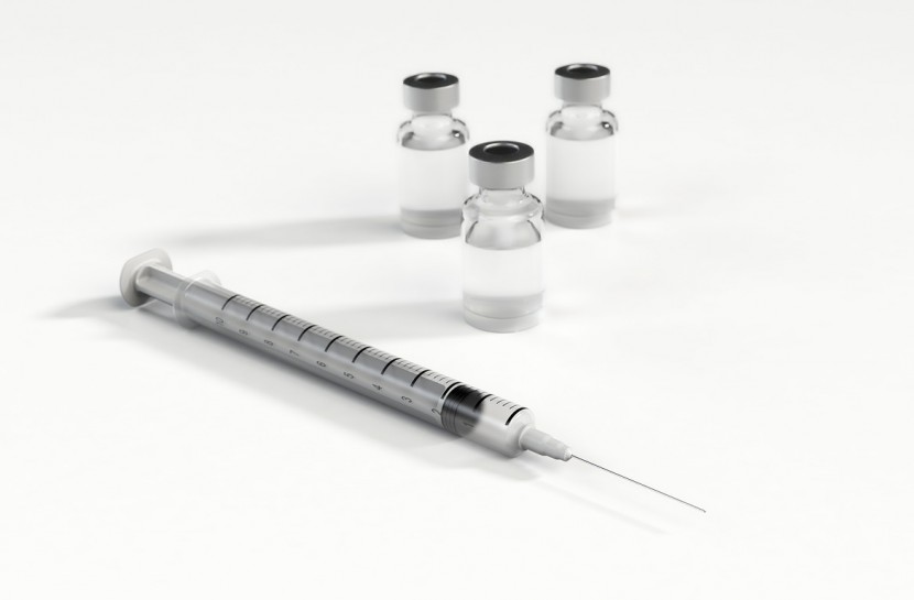 Foto em fundo branco com uma seringa e três frascos de vacina.
