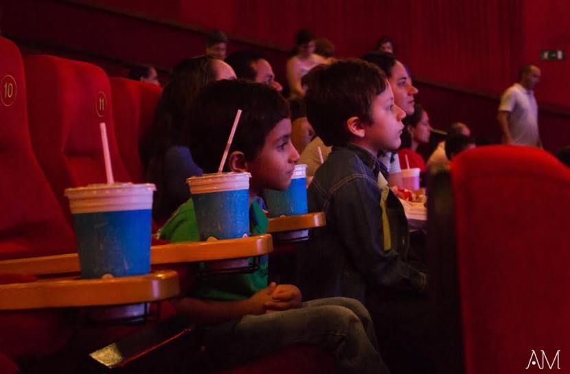Foto de uma sala de cinema com duas crianças olhando em direção da tela.