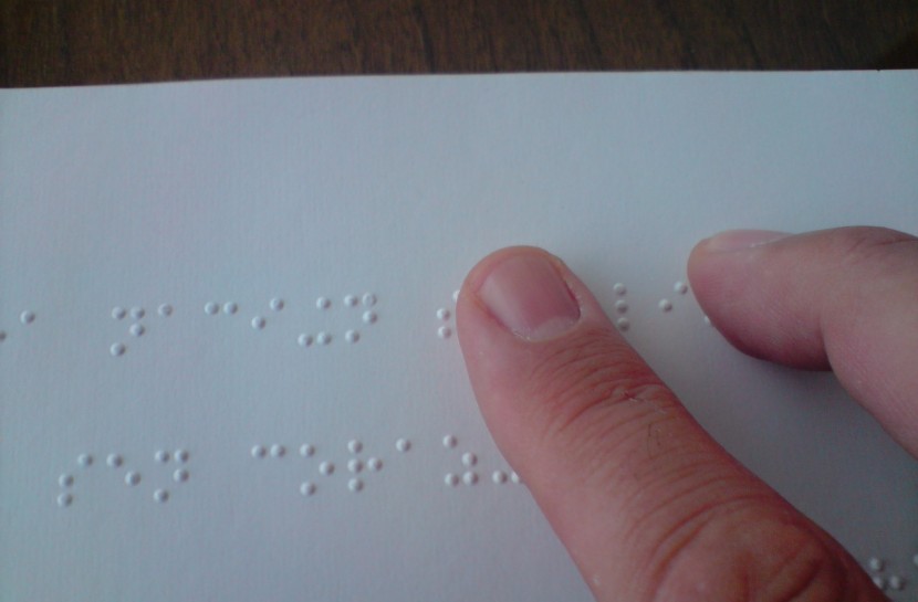 Foto mostra dedos em close, tateando um texto em braille.