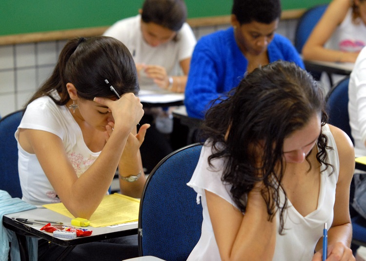 Foto de uma sala de aula, com diversos jovens sentados em carteiras, durante aplicação da prova do Enem