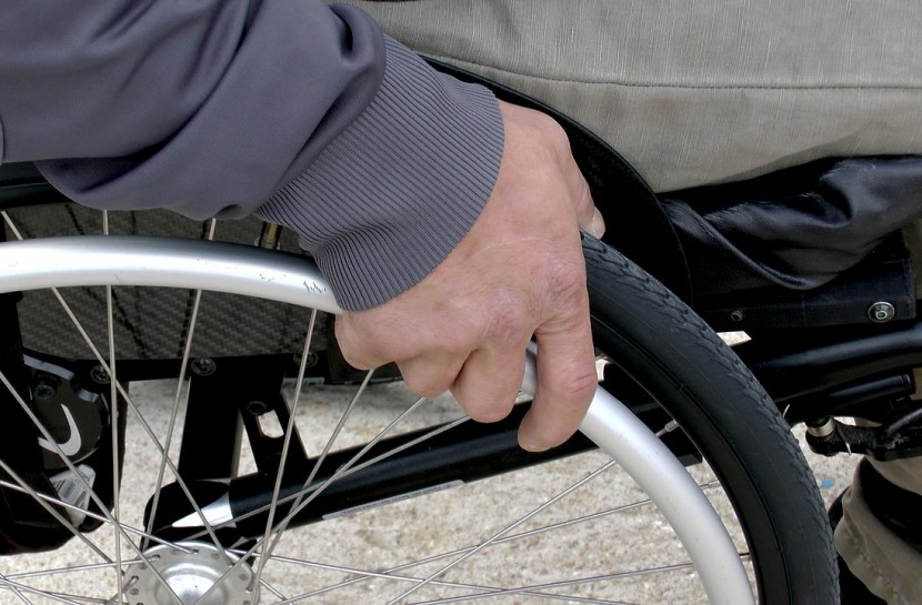 Foto de um homem sentado em uma cadeira de rodas. Uma das mãos dele segura aro de impulsão da cadeira de rodas.