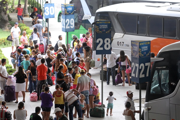 Foto em plano geral de um terminal rodoviário; há um ônibus estacionado e muitas pessoas embarcando na plataforma