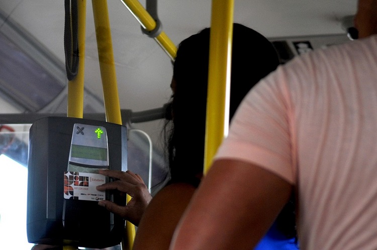 Foto de uma mulher passando o cartão especial no leitor do ônibus