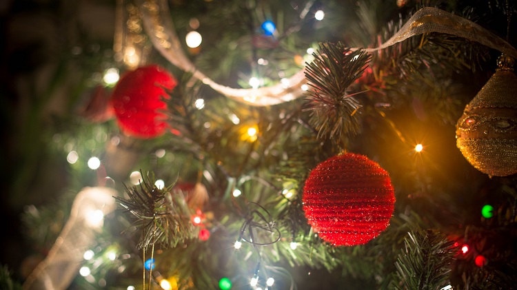 Foto do detalhe de uma árvore de natal, com bolas natalinas de linha vermelha e pisca-pisca