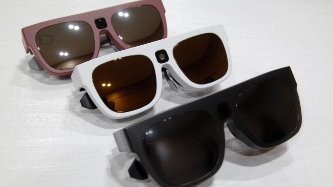 Foto de três óculos inteligentes. Eles possuem lentes escuras e retangulares, com opções de armações em rosa, branca e preta.