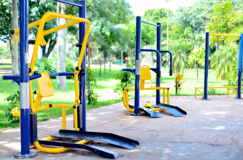 Foto de três equipamentos de musculação adaptados para cadeirantes em uma praça ao ar livre