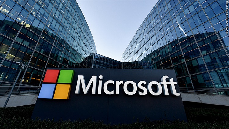 Fachada de dois prédios espelhados, com o logo da Microsoft em destaque. quatro quadrados - vermelho, verde, azul e amarelo formam uma janela. Ao lado, há a palavra Microsoft em branco