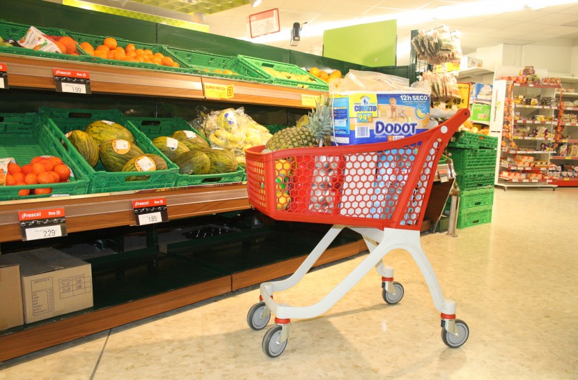Foto de um carrinho plástico vermelho carregado de compras parado na seção de hortifruti de um supermecado