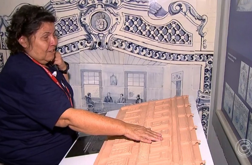 Foto de uma senhora cega tateando réplicas em relevo dos desenhos de azulejos portugueses