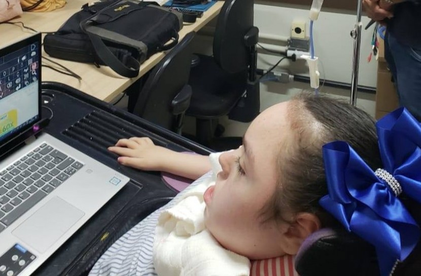 Uma adolescente em cadeira de rodas e aparelho respiratório, com um notebook a frente, na altura dos olhos