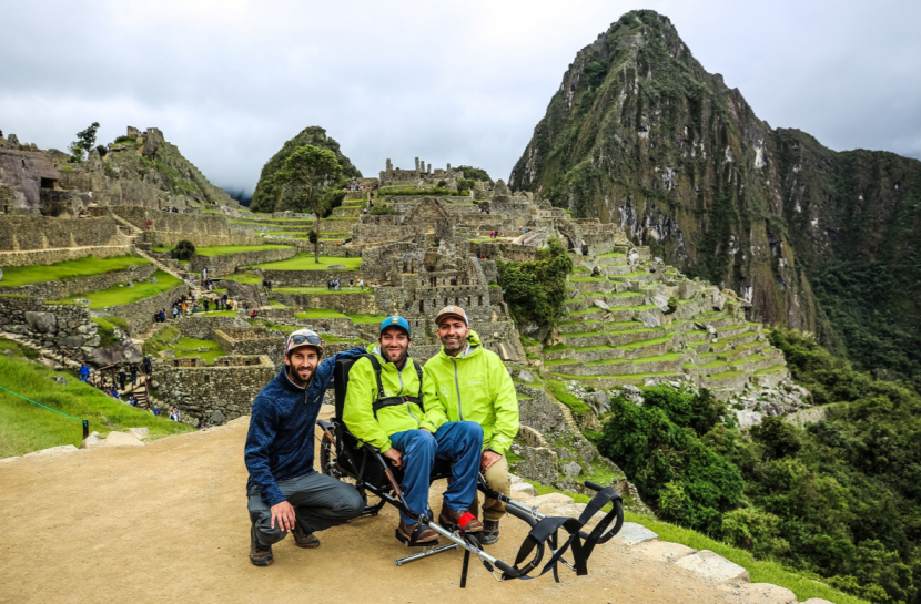 Foto em plano aberto com três amigos e a cidade dos incas ao fundo. Ao centro, está um homem em