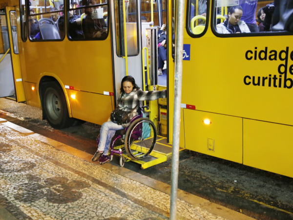 Mulher jovem na cadeira de rodas descendo de um ônibus.