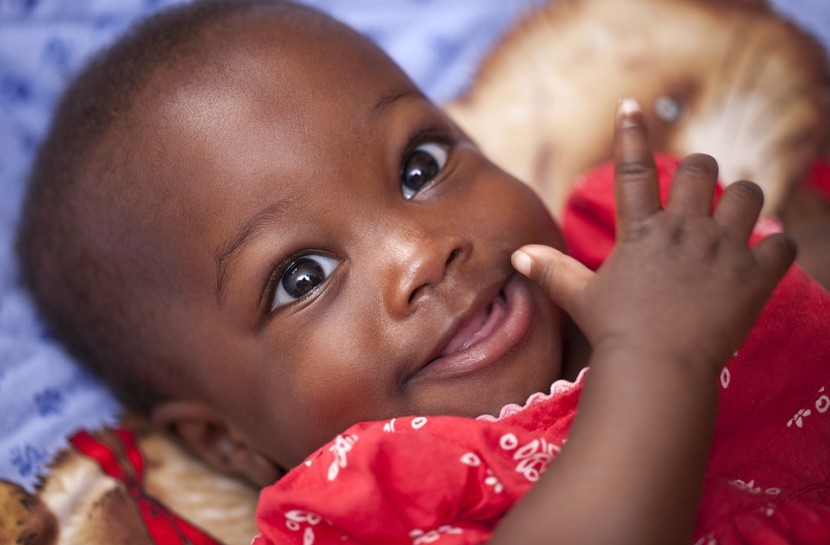 Foto de uma bebê negra, sorrindo, com grandes olhos castanhos