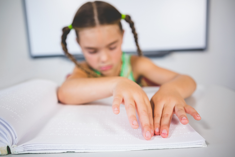 Foto de uma menina de aproximadamente 7 anos lendo em braile