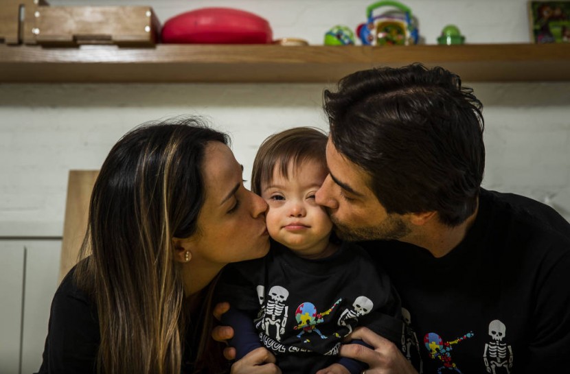 Foto da família Zylberstanj. No centro, o pequeno Pepo, entre a mãe, Marina e o pai, Henry. Ambos estão de rostos virados, beijando, ao mesmo tempo, as bochechas do filho.
