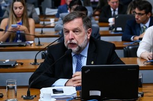 Foto do senador Flávio Arns sentado falando ao microfone com um notebook na sua frente.