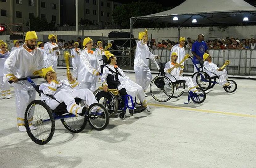 Foto de um grupo de pessoas fantasiadas, sendo que alguns são cadeirantes e estão sendo conduzidos por outras pessoas