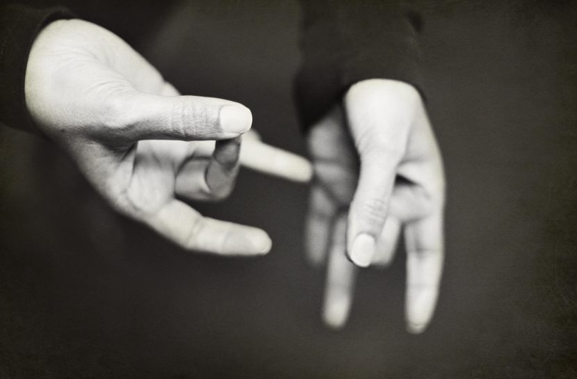 Foto em branco e preto, fundo escuro, com mãos fazendo o sinal de especial na língua de sinais