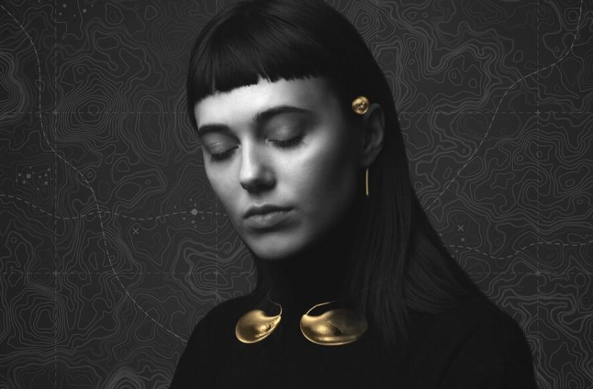 Foto em branco e preto da Sophie Harrocks de olhos fechados, com detalhes dourados do Sensaura na sua orelha esquerda e pescoço.