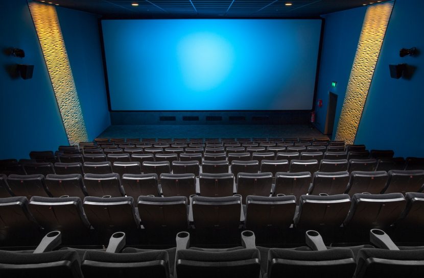 Imagem de uma sala de cinema vazia, com poltronas pretas em formato de arquibancada.
