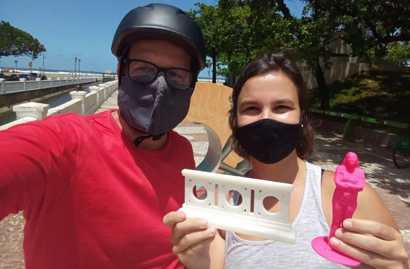 Foto em estilo selfie de Renato Frosch ao lado de uma mulher. Ela segura dois monumentos impressos em 3D