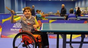 Foto de um garoto em uma cadeira de rodas jogando tênis de mesa