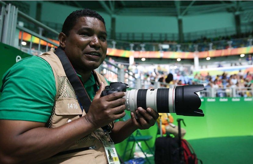 Foto de João Maia de perfil segurando uma máquina fotográfica nas mãos durante a cobertura dos Jogos Paralímpicos do Rio de Janeiro em 2016