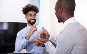Foto de dois homens negros em um escritório. Eles usam roupas sociais e falam por meio de língua de sinais