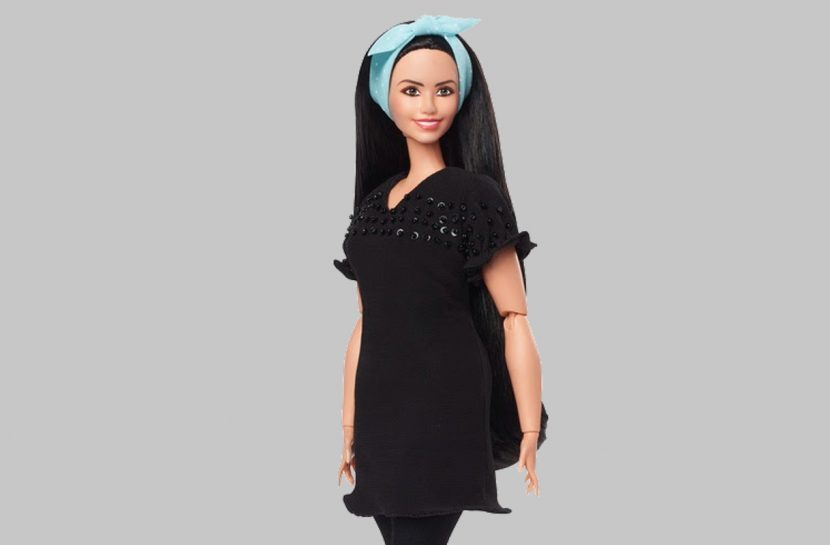 Foto da boneca Barbie Doani Emanuela Bertan. Ela tem pele branca, cabelos longos, abaixo da linha da cintura, lisos e escuros e usa uma faixa azul na cabeça e um vestido preto.