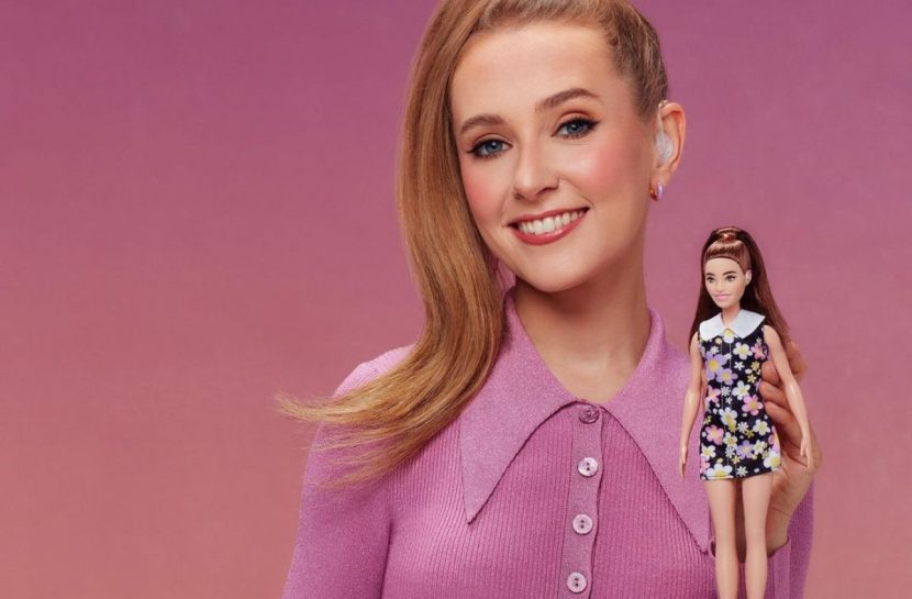 Foto posada da atriz Rose Ayling-Elis com a boneca surda e com aparelho auditivo da Mattel nas mãos.