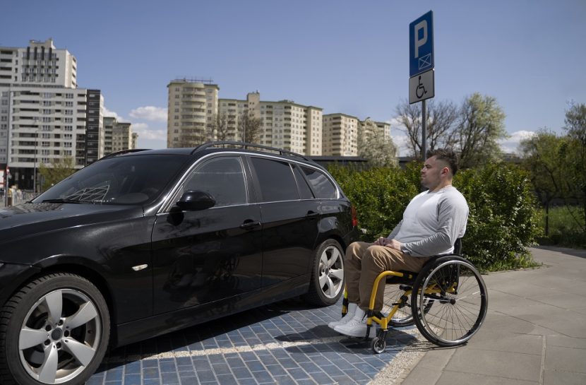 Foto de um cadeirante parada ao lado de um carro estacionado.
