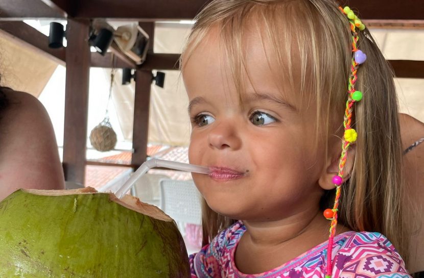 Foto de uma criança com nanismo que toma água de coco com um canudo.